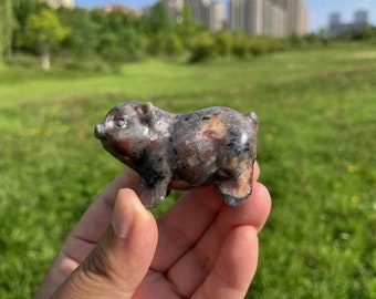 May include: A small, hand-carved pig figurine made of a dark gray and pink speckled stone. The pig is standing on all four legs and has a slightly upturned snout.