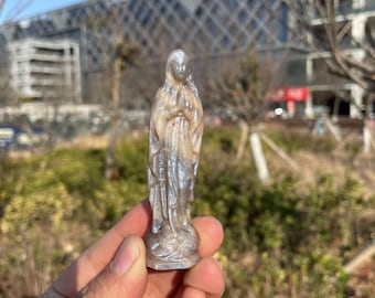 Könnte beinhalten: Eine kleine, weiße und schimmernde Figur der Jungfrau Maria mit gefalteten Händen zum Gebet. Die Figur ist aus einem durchscheinenden Material gefertigt, das im Licht glänzt.