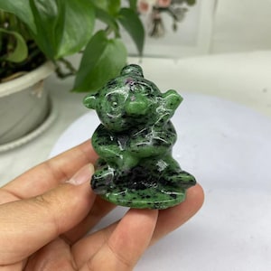 May include: A green and black carved stone figurine of a sitting animal with large eyes. The figurine is made of a type of gemstone called green aventurine.