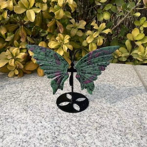 May include: A green and pink butterfly figurine made of stone, mounted on a black metal stand.
