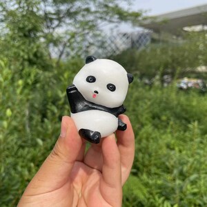 May include: A white and black panda-shaped squishy toy with a pink tongue sticking out. The toy has black eyes and a black nose.