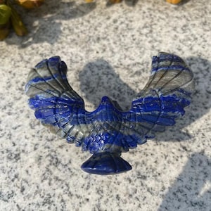 May include: A carved lapis lazuli eagle sculpture with wings spread wide. The eagle is a symbol of freedom, strength, and power.