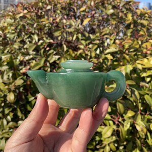 Könnte beinhalten: Eine kleine grüne Jade-Teekanne mit Deckel. Die Teekanne ist in Form einer traditionellen chinesischen Teekanne geschnitzt.