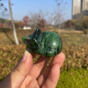 May include: Green and pink gemstone carved into the shape of a sleeping cat. The cat is lying on its side with its head resting on its paws.
