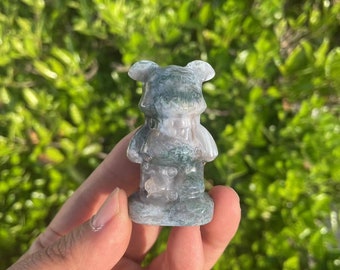 Puede incluir: Una talla de ágata verde y blanca de una pequeña criatura de dibujos animados con cabeza redonda y orejas grandes. La talla es detallada y tiene un acabado liso y pulido.
