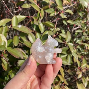 Puede incluir: Una figurita de ardilla tallada en ágata con un esquema de color rosa y blanco. La ardilla está sentada sobre sus  haunches con la cola enroscada detrás de ella.