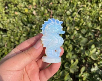 May include: A white opal seahorse figurine with iridescent details. The figurine is carved in a standing position with its tail curled.