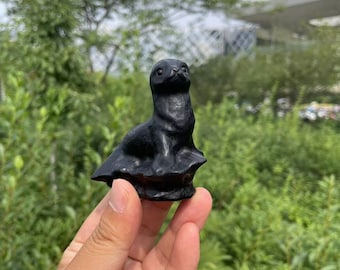 May include: A black obsidian sculpture of a seal, sitting on a rock base. The sculpture is about 5 inches tall and is a popular choice for home decor.