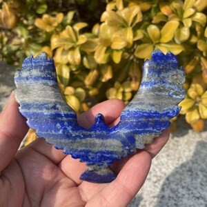 May include: A blue and gray lapis lazuli eagle carving. The eagle is carved in a flying pose with its wings spread wide.