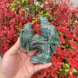 May include: A green and pink carved stone sculpture of two birds perched on a branch. The sculpture is made of a type of gemstone known as green aventurine.