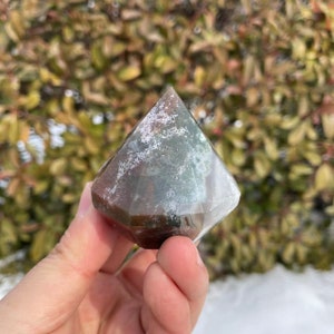 May include: A green, brown, and white agate gemstone carved into a diamond shape. The gemstone is polished and has a smooth surface.