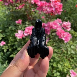 May include: A black resin figurine of a hooded figure sitting with its hands clasped in its lap.