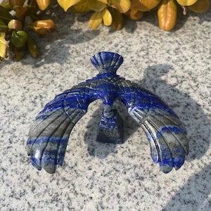 May include: A blue and grey carved lapis lazuli eagle sculpture with outstretched wings.