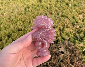 May include: A pink seahorse carved from a crystal. The seahorse is standing on a flat base and has a detailed design.