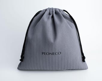 May include: A grey drawstring pouch made of fabric with black cords. The front of the bag features the text PEONECO printed in a simple black font. The bag has a gathered top closure and a smooth, uniform texture across the entire surface.