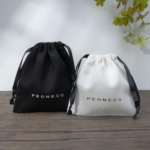 May include: Two drawstring pouches, one black and one white, sit side-by-side on a wooden surface. Each pouch has a black drawstring and the word "PEONECO" printed in white. The white pouch is made of a canvas-like material.