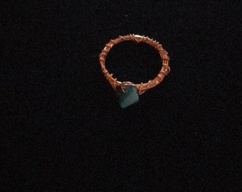 Puede incluir: Un anillo de alambre de cobre con una piedra verde oscura en el centro.