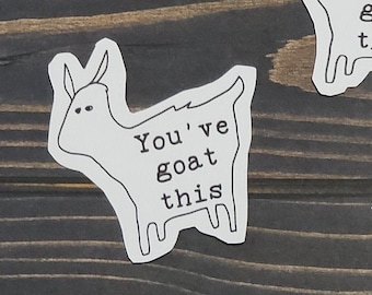 May include: Three white goat stickers on a dark wood background. Each sticker has a black outline and the text "You've goat this".