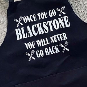 May include: Black apron with white text that reads "Once you go Blackstone you will never go back" with a spatula and fork graphic on each side of the text.
