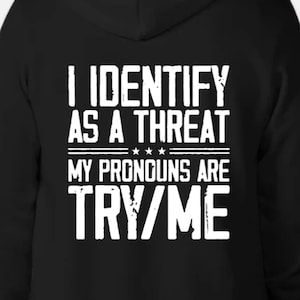 May include: Black hoodie with white text that reads "I identify as a threat. My pronouns are try/me."