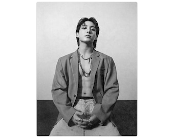 May include: Black and white portrait of a person wearing a gray blazer, light-wash denim jeans, and layered necklaces. The person is seated with hands clasped, and the blazer is unbuttoned, revealing the torso.