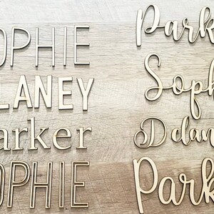 May include: Eight wooden name signs with the names Sophie, Delaney, and Parker. The names are in different styles and fonts. The signs are numbered 1 through 8.