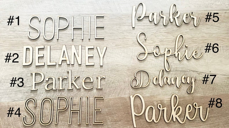 May include: Eight wooden name signs with the names Sophie, Delaney, and Parker. The names are in different styles and fonts. The signs are numbered 1 through 8.