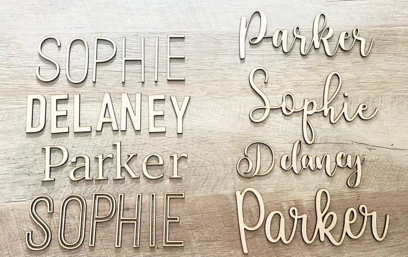 May include: A set of wooden name signs with the names "Sophie", "Delaney", and "Parker" in different styles. The names are cut out of wood and have a natural finish.