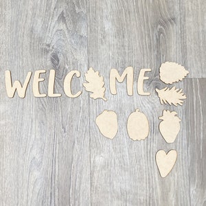 May include: Wooden cutout letters spelling "WELCOME" with various wooden cutouts of leaves, acorns, pumpkins, strawberries, and a heart.