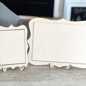 May include: Two wooden picture frames with ornate edges and easel backs. The frames are blank and ready to be decorated.