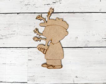 May include: A wooden cutout of a person wearing a hat with antlers, holding a book. The cutout is in a standing position and is made of light brown wood. The antlers are detailed and extend from the hat.