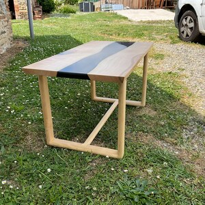 Op de afbeelding: Een houten salontafel met een zwart epoxy rivierontwerp. De tafel heeft een eenvoudig, modern ontwerp met een rechthoekig blad en een metalen frame.