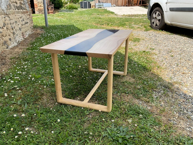 Op de afbeelding: Een houten salontafel met een zwart epoxy rivierontwerp. De tafel heeft een eenvoudig, modern ontwerp met een rechthoekig blad en een metalen frame.
