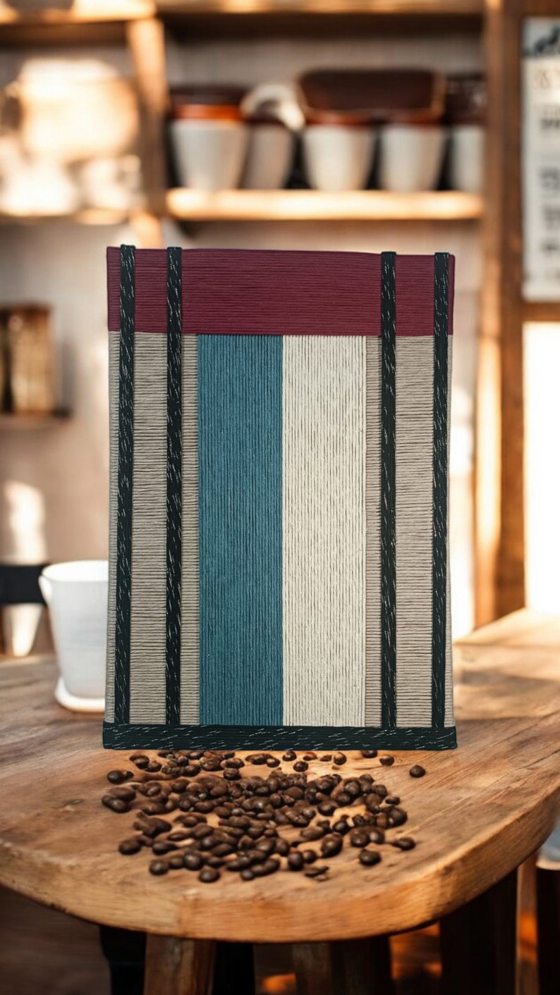 May include: A striped fabric tote bag with a burgundy top, black trim, and a white, blue, and beige striped pattern. The bag is sitting on a wooden table with coffee beans scattered around it.