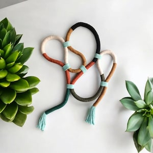 May include: A long, multi-coloured cord necklace with tassels on each end. The cord is made of different coloured yarns, including black, brown, white, green, and blue.