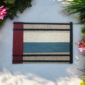 May include: A woven placemat with a red, cream, and blue striped design. The placemat has black trim and is made of natural fibers.