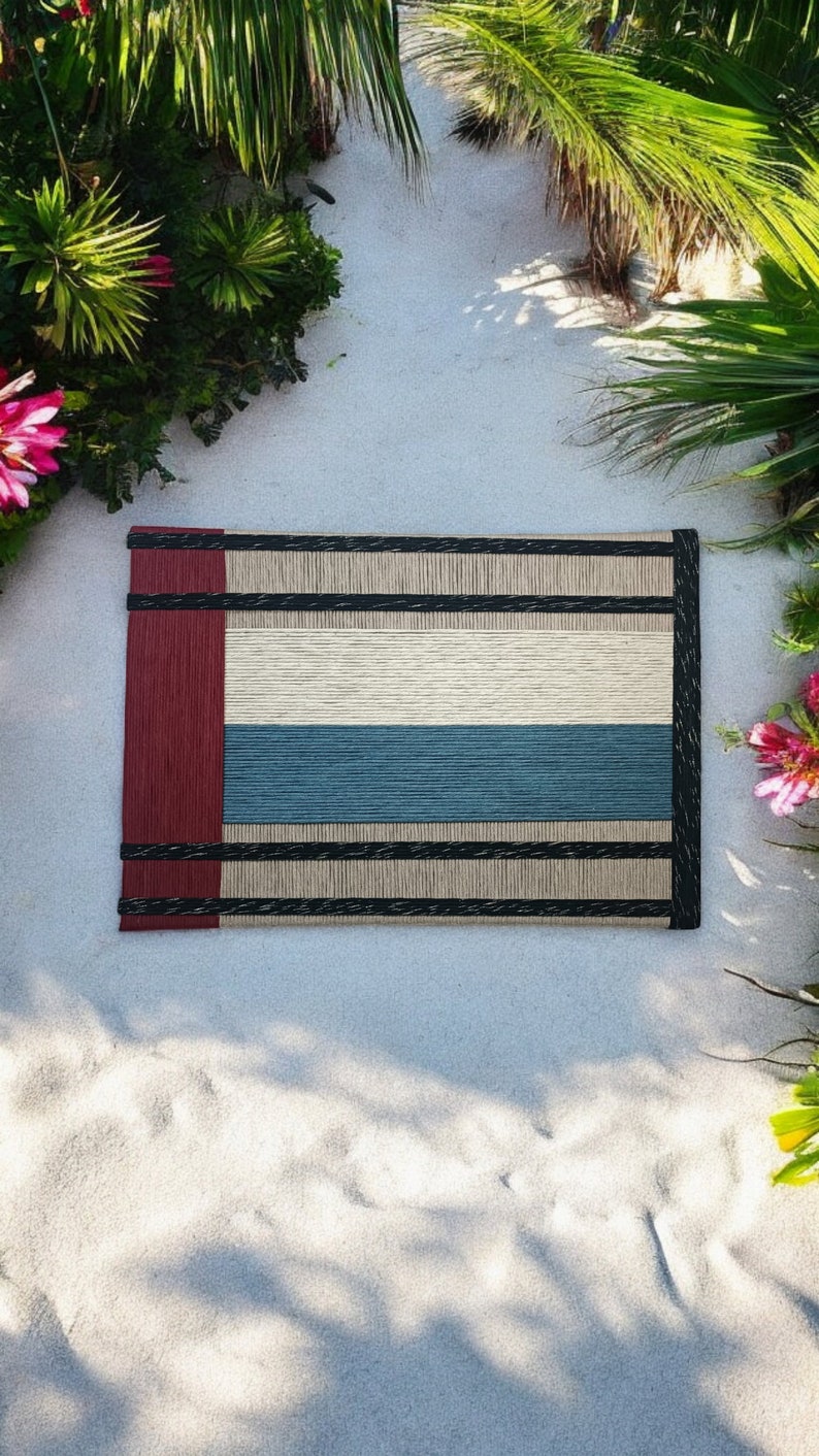 May include: A woven placemat with a red, cream, and blue striped design. The placemat has black trim and is made of natural fibers.
