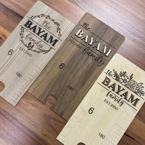 May include: Three wooden growth charts with the text "the Bayam family est. 1990" in different styles. The charts have a ruler on the side with markings in inches and centimeters.