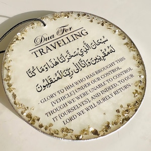 Op de afbeelding: Ronde witte auto-luchtverfrisser met gouden glitter ingebed in de hars. De luchtverfrisser heeft zwarte tekst die "Dua For Travelling" luidt en een Arabisch gebed in zwarte tekst.