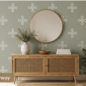 Op de afbeelding: Een saliegroene muur met een herhalend wit geometrisch patroon, een ronde spiegel en een lichthouten dressoir met rieten deuren. Op het dressoir staat een witte vaas met groen, een houten kom en een stapel witte boeken. De tekst Entryway is zichtbaar.