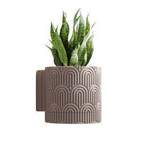 May include: A cylindrical, light brown planter with a repeating arch design, holding a snake plant with green and yellow striped leaves. The planter has a bracket for wall mounting. A decorative item for home decor.
