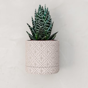 May include: A set of three ceramic mugs with a speckled, matte finish. The mugs are in shades of cream, light gray, and dark gray. Each mug has a simple, minimalist design and a rounded handle.