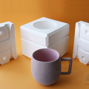 May include: Three white ceramic molds for making a mug, with a light purple mug in the center.