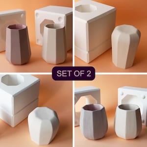 以下が含まれることがあります： ピンク、ベージュ、グレーなど、さまざまなニュートラルカラーの幾何学的なセラミック花瓶2個セット。 花瓶はファセットデザインで、白い型と一緒に表示されています。「SET OF 2」の文字が見えます。