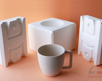 May include: Three white ceramic molds for making a mug. The molds are in the shape of a cube and two rectangles. A white ceramic mug is in the center of the image.
