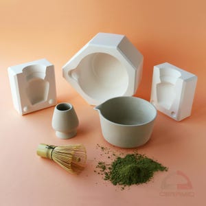May include: A collection of matcha tea preparation tools, including a bamboo whisk, a ceramic bowl, a matcha powder, and a small tea cup. The background is a light orange color.
