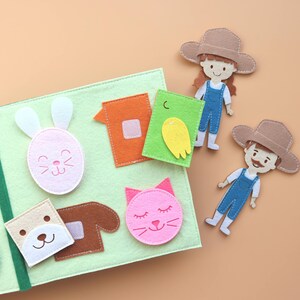 May include: A felt activity book with various shapes and characters, including a bunny, a cat, a house, a bird, and two people. The book is green and has a brown border.