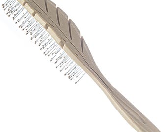 Può includere: Una spazzola per capelli in plastica beige con un design a forma di foglia e una fila di setole metalliche.