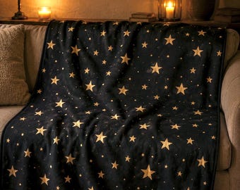 Puede incluir: Una manta negra con un patrón de estrellas doradas, colocada sobre un sofá. La manta presenta estrellas doradas de varios tamaños dispersas sobre la tela oscura. Hecha de un material suave, es adecuada para la decoración del hogar.