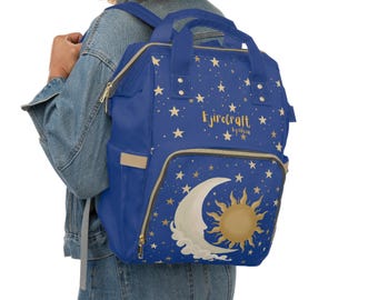 Puede incluir: Una mochila azul con un patrón celestial de estrellas doradas, una luna creciente y un sol. El texto Ejirocraft by olivia está impreso en dorado en la parte frontal. La mochila incluye asas superiores, un bolsillo frontal y bolsillos laterales.
